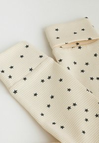 Chaussettes en tissu texturé couleur crème avec des motifs d’étoiles noires uniformément dispersés sur toute la surface.