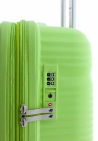Maleta dura verde con estrías verticales, tiradores grises dobles en el zipper y un candado de combinación de tres dígitos que presenta un símbolo de la TSA.