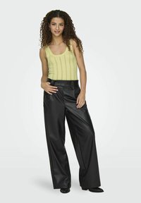 Lichtgele geribde tanktop gecombineerd met licht hoge zwarte faux leren wijde broek, met een riem met een eenvoudige gesp.