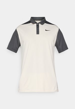 Polo de Nike en beige y gris oscuro, con cuello abotonado, mangas cortas y un sutil logo en el pecho. Textura suave.