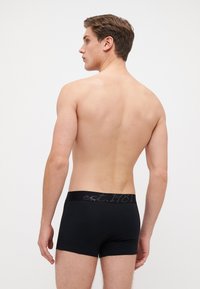 Svarte boxer shorts med bred elastisk midjebånd som har grå tekst. Shortsene er tettsittende, laget av et mykt materiale, og har en glatt overflate.