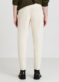 Cream-colored trousers made from textured fabric, featuring two back pockets and a tailored fit, paired with black ankle boots.