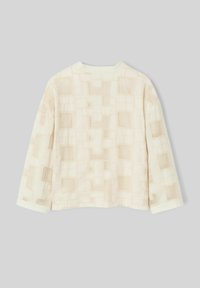 Veste couleur crème avec un motif texturé en grille présentant des carrés en relief. Les manches longues et le col rond complètent le design.