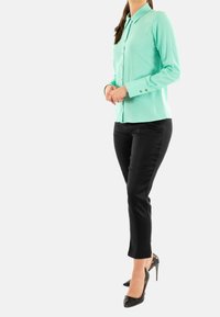 Camicia verde menta con bottoni, maniche lunghe e hardware argentato, abbinata a pantaloni neri slim-fit e tacchi alti neri.