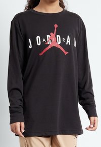 Svart långärmad skjorta i bomull med en röd Jumpman-logga i mitten och texten "JORDAN" i vita bokstäver.