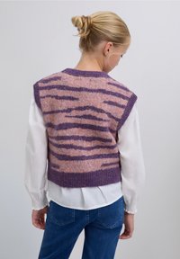 Jersey sin mangas de punto con un patrón de rayas de tigre en rosa y púrpura, con un acabado texturizado y un escote redondo, usado sobre una blusa blanca.