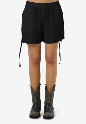 Schwarze, leichte Shorts mit einem elastischen Bund, seitlichen Taschen und verstellbaren Bindebändern am Saum, kombiniert mit grünen und schwarzen Cowboy-Stiefeln.