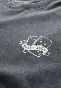 Tricou din țesătură gri închis, cu un grafic alb uzat reprezentând cărți de joc, având inscripția "MERRY XMAS" într-un design de panglică.
