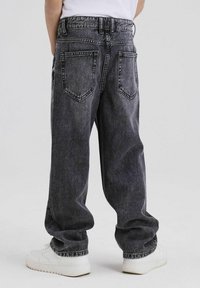 Donkergrijze denim jeans met een relaxte pasvorm, voorzien van een hoge tailleband, vijf zakken en zichtbare stiksels, gecombineerd met witte sneakers.