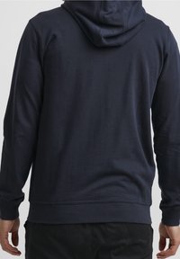 Sweat à capuche bleu marine avec une texture douce, une capuche à cordon, des manches longues et des poignets et ourlets côtelés, présentant un design simple et épuré.