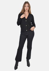 Cardigan nero con bottoni, maniche lunghe e scollo a V. Abbinato a jeans a zampa d'elefante scuri e stivaletti neri con tacco. Tessuto morbido.