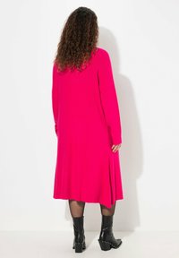 Robe fuchsia à manches longues avec fentes latérales, fabriquée à partir d'un tissu lisse. Portée avec des bottes noires à talons jusqu'aux genoux ornées d'éclats.