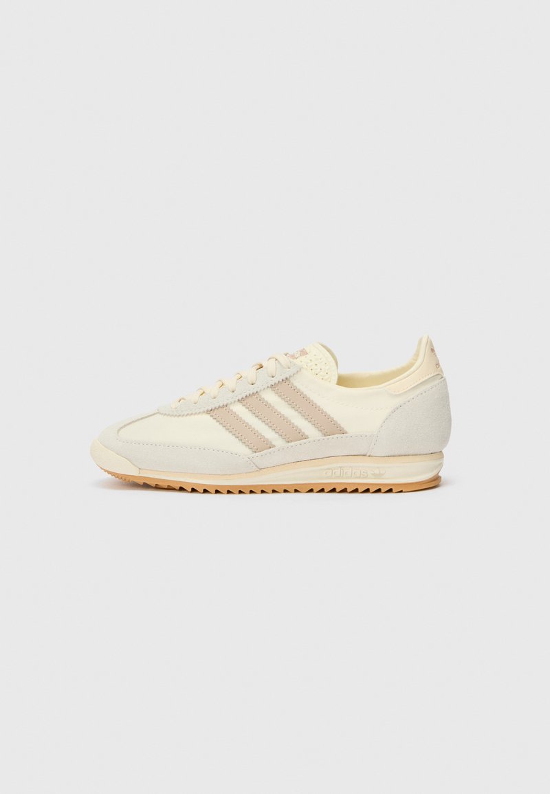 Kremowe sportowe sneakersy z trzema beżowymi paskami, wykonane z zamszu i materiałów tekstylnych, z teksturowaną podeszwą oraz wytłoczonym logo na pięcie.