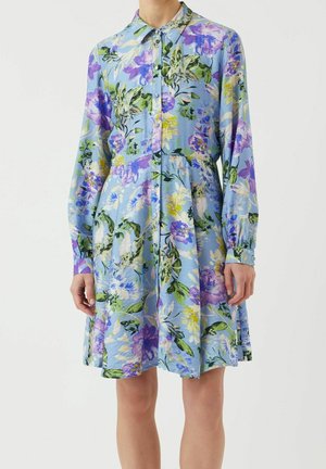 Robe chemise bleu clair à manches longues, avec un motif floral vif en violet, vert, jaune et blanc.