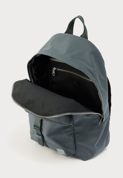 Γκρι νάιλον σακίδιο πλάτης με φερμουάρ, εσωτερική θήκη και ρυθμιζόμενο λουρί. Λείο υλικό, μινιμαλιστικός σχεδιασμός.