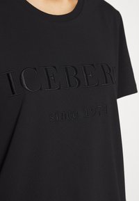 Camiseta de algodón negra con cuello redondo, que presenta texto en relieve "ICEBERG" y "desde 1974" en un acabado tonal. Manga corta.