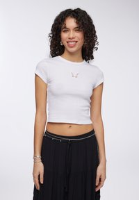 T-shirt bianco corto realizzato in materiale ribbed, con un design a forma di farfalla ritagliato sul petto. Maniche corte e silhouette aderente.