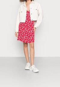 Red floral print dress with a deep neckline, paired with a cropped white denim jacket and white sneakers. Smooth fabric, casual design.