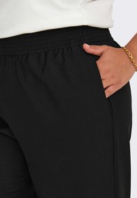 Μαύροι joggers με ελαστική μέση, πλευρικές τσέπες, μαλακό ύφασμα και άνετη εφαρμογή. Λεπτομέρεια από κοντά της μέσης και της τσέπης.