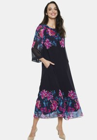 Granatowa sukienka w kwiaty z prześwitującymi rękawami, z jasnoróżowymi i niebieskimi kwiatami przy dolnej krawędzi. Luźny fason z dwiema bocznymi kieszeniami.