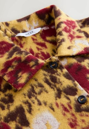 Wool shirt with a leopard print pattern in yellow, red, and brown. Features a collar and black buttons, textured, soft fabric.
