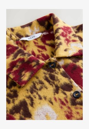 Chemise en laine avec un motif léopard en jaune, rouge et marron. Dotée d'un col et de boutons noirs, tissu texturé et doux.