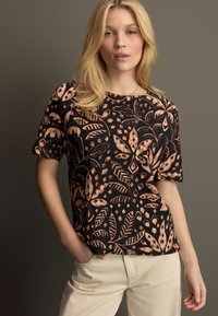 Top noir à manches courtes avec un motif floral et de feuilles dans des teintes brunes. Coupe décontractée, col rond et tissu léger.