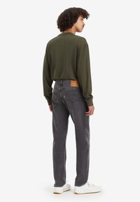 Jeans negri închis, cu tăietură dreaptă, având o petică din piele pe spate. Asortați cu o cămașă cu mânecă lungă de culoare verde măsliniu și teniși albi.