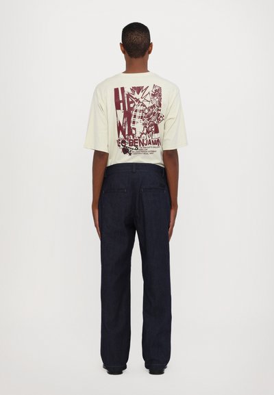 Helle Grafik-T-Shirt mit marmoriertem Druck auf der Rückseite, kombiniert mit dunklen Jeans mit geradem Schnitt und dezenten Nähdetails.