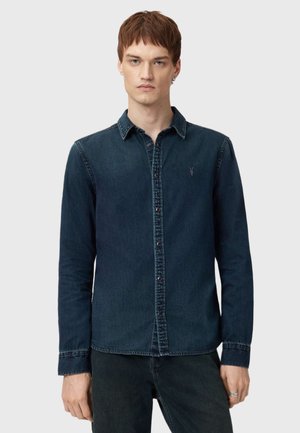 Donkerblauwe spijkerblouse met lange mouwen, knoopsluiting aan de voorkant en een puntige kraag. Heeft vervaagde randen en een klein geborduurd logo op de borst.