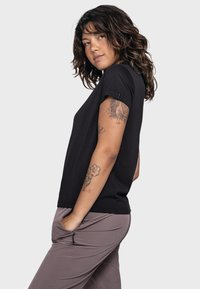 Schwarzes Baumwoll-T-Shirt mit körperbetonter Passform, kurzen Ärmeln und einem leicht gerundeten Halsausschnitt, kombiniert mit hellgrauen Hosen mit seitlichen Taschen.