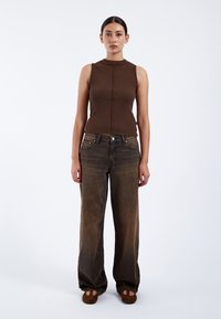 Top sans manches côtelé brun avec un col haut, associé à un jean brun délavé à coupe ample et des mocassins en daim brun.
