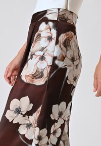 Bloemmotief rok van een satijnachtige stof. Beschikt over bruin en crèmekleuren met een soepele textuur en een geplooid ontwerp in de taille.