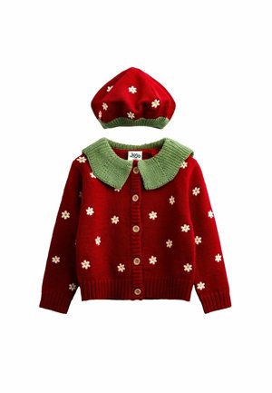 Rode gebreide cardigan en bijpassende baret met witte bloemenpatronen en groene kragen en biezen, plat neergelegd op een witte achtergrond.