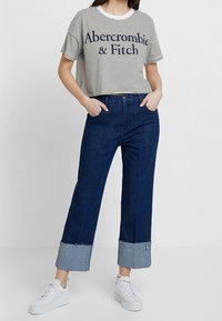 Zkrácený pruhovaný tričko s námořnickými a bílými pruhy, se značkou "Abercrombie & Fitch". Tmavě modré široké džíny s denimovými manžetami. Bílé tenisky.