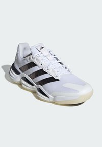 Weißer Sportschuh mit einem Obermaterial aus Mesh, drei schwarzen Streifen und einer strukturierten Sohle. Verfügt über einen gepolsterten Schaft und markante, geformte Akzente.