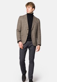 Brązowa kratkowana marynarka na czarnym golfie, połączona z szarymi spodniami w kratę. Gładki materiał, dopasowany krój, jednorzędowy fason.