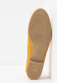 Semelle d'une chaussure jaune perforée avec une semelle en caoutchouc étiquetée "SOFT FLEX" et des indications de taille, présentée à la verticale sur fond blanc.
