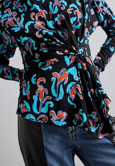 Black top with colorful floral pattern in turquoise and red, featuring a twisted front design. Paired with dark jeans for a contrast.