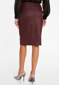 Femme portant une jupe crayon à rayures bordeaux et des chaussures à talons aiguilles argentées étincelantes, vue de dos.