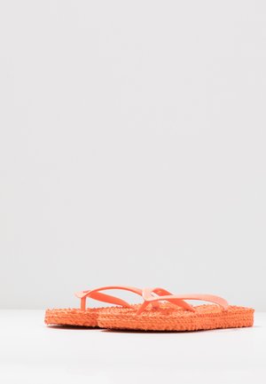 Par de chanclas tejidas naranjas con tiras delgadas colocadas sobre una superficie blanca contra un fondo liso.