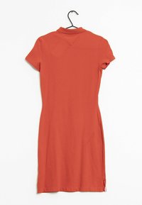 Kurzärmliges, tailliertes Kleid aus Terrakotta-Stoff, mit Polokragen, seitlichen Schlitzen und glatter Textur, hängt an einem schwarzen Haken.