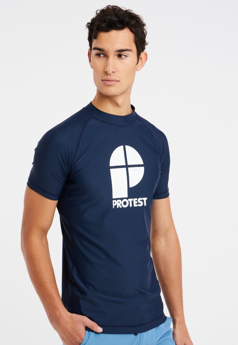 Námořnická modrá rash guard tričko vyrobené z hladkého, elastického materiálu. Obsahuje bílé logo tištěné na přední straně a krátké rukávy.