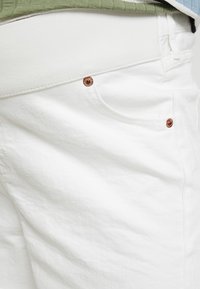 Vita bomullsshorts med en mjuk textur, försedda med kopparfärgad hårdvara och en sidficka. Midjebandet har en enkel, enfärgad design.