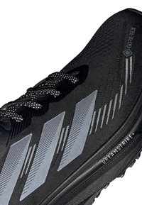 Scarpa sportiva nera con strisce riflettenti argento, lacci a fantasia, etichetta Gore-Tex e "Dreamstrike+" stampato sul bordo della suola.