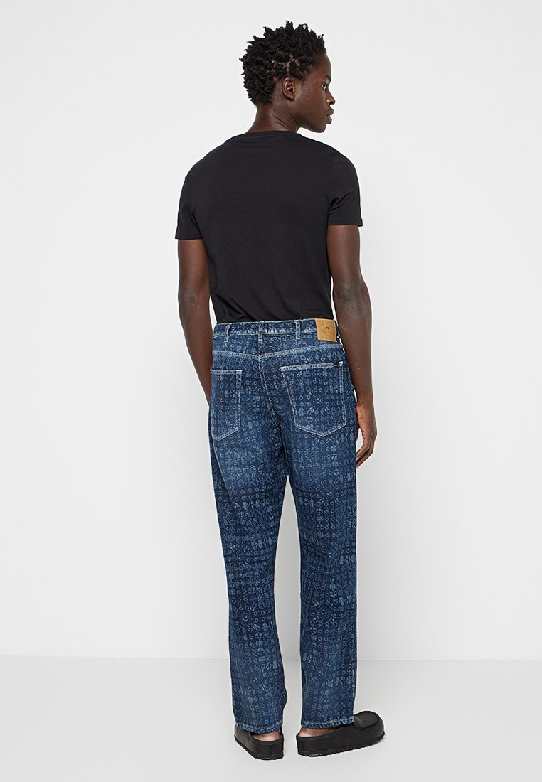Jeans denim w ciemnoniebieskim wzorze, z medium rise, prostymi nogawkami oraz łatą na tylnej banderze. Na sobie czarny t-shirt.