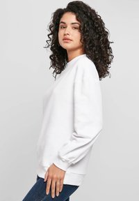 Valkoinen puuvillainen collegepaita, jossa on pitkät, liehuvat hihat ja pyöreä pääntie. Sileä pinta, rento istuvuus sekä resorit hihansuissa ja helmassa.