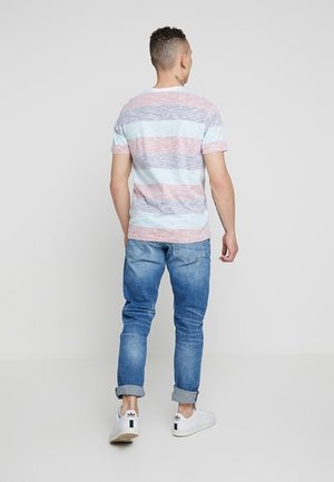 Tęczowy t-shirt z krótkim rękawem w pastelowych kolorach z jasnoniebieskimi, różowymi i białymi paskami; noszony z jasnoniebieskimi dżinsami i białymi sneakersami.