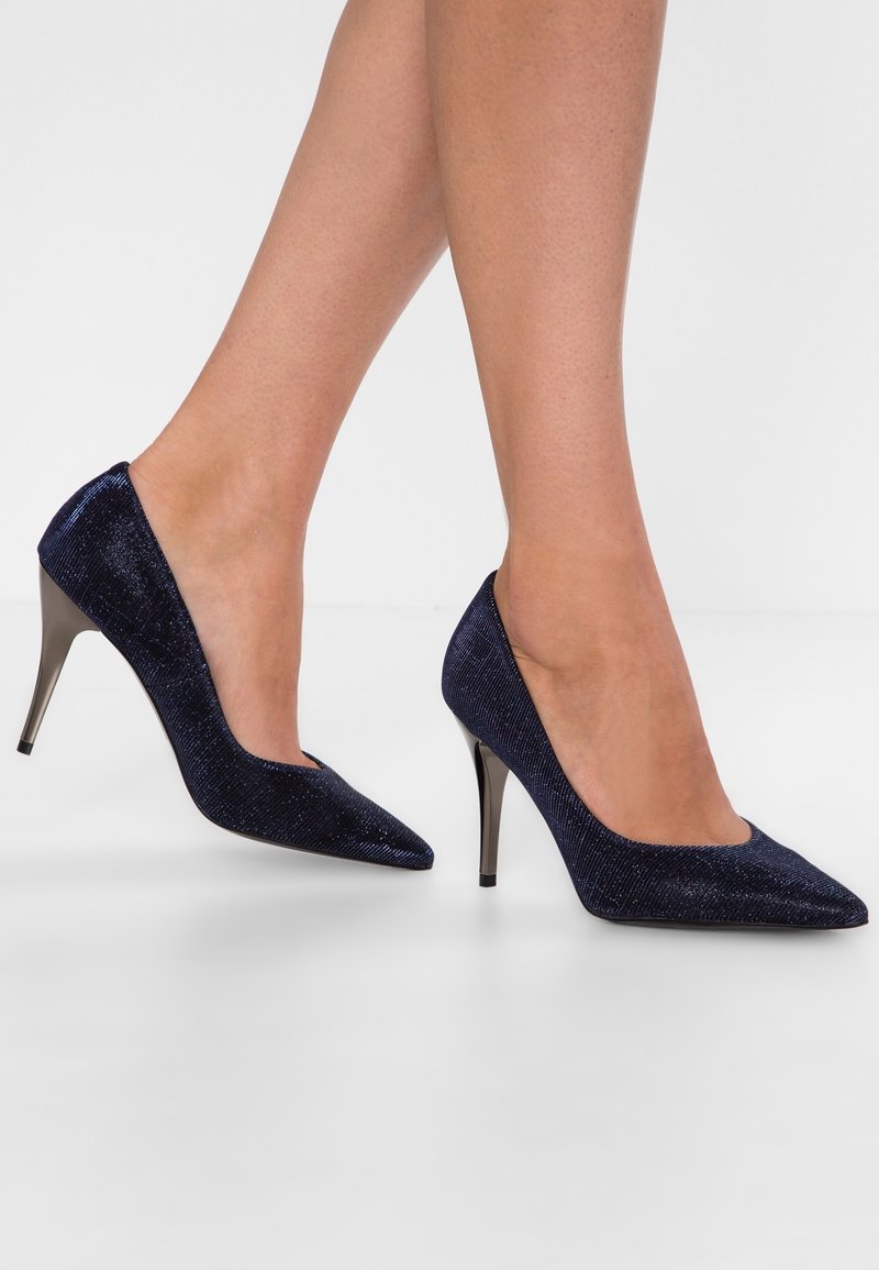 Chaussures à talons hauts bleu marine avec bout pointu, tissu texturé et accent métallique brillant sur le talon.