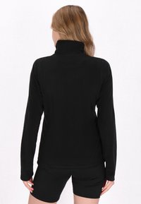 Sort langærmet top med høj krave, lavet af glat stof. Har tætsiddende design og flade sømme, parret med sorte shorts.